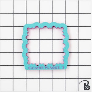 May include: A turquoise blue and purple square plaque cookie cutter with a scalloped edge. The cutter is on a white grid background. The text "SQUARE PLAQUE 3" is printed on the cutter.