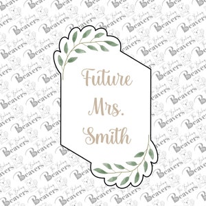 May include: A white hexagonal sign with a leafy green border. The sign says "Future Mrs. Smith" in a light brown font.