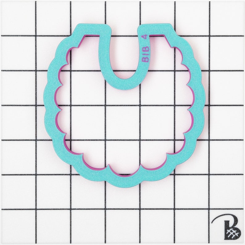 May include: A teal and purple bib-shaped cookie cutter with a scalloped edge. The text "BIB 4" is printed on the top right side of the cutter. The cutter is made of plastic and is set against a white grid background.