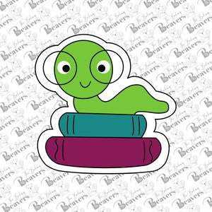 May include: A green worm wearing glasses sits on top of a stack of two books. The top book is teal blue and the bottom book is purple. The worm has a happy expression on its face.