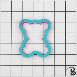 May include: Teal blue teddy bear cookie cutter with a pink outline. The cutter has the words "Teddy Bear" inscribed around the edge.