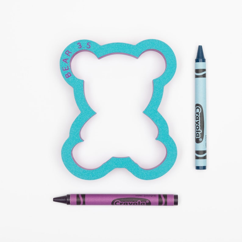 May include: A blue foam bear-shaped cookie cutter with the text "BEAR 3.5" on the side. Two crayons, one blue and one purple, are next to the cookie cutter.