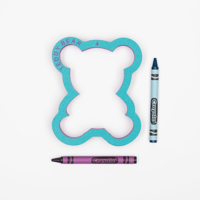 May include: A turquoise blue teddy bear shaped cookie cutter with the words "Teddy Bear 4" around the edge. Two crayons, one blue and one purple, are next to the cookie cutter.