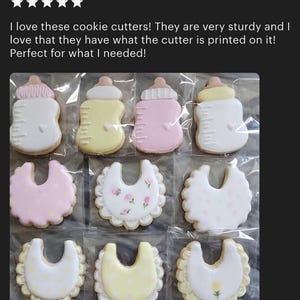 May include: A selection of baby-themed biscuits, featuring bottle and bib designs, adorned with pastel hues and delicate decorations. The biscuits are individually wrapped and neatly arranged. The text "Ruffled Baby Bib Cookie Cutter" is visible.