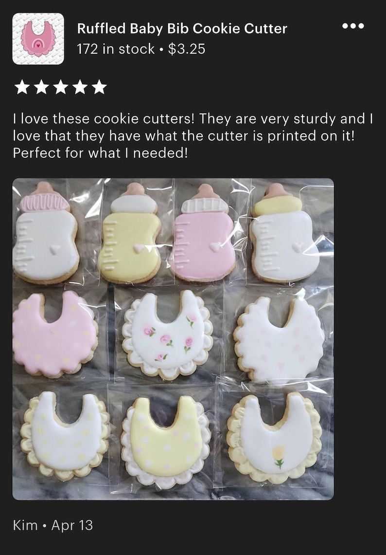 May include: A selection of baby-themed biscuits, featuring bottle and bib designs, adorned with pastel hues and delicate decorations. The biscuits are individually wrapped and neatly arranged. The text "Ruffled Baby Bib Cookie Cutter" is visible.