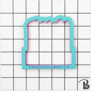 K&ouml;nnte beinhalten: Ein t&uuml;rkisblauer und rosafarbener Keksausstecher aus Kunststoff in Form eines Rechtecks mit einer gewellten Oberkante. Der Ausstecher hat den Text "CANDLE PLAQUE 3.5" auf der Unterkante aufgedruckt.