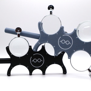 May include: A set of two lens holders for eye exams. The holders are made of black and gray plastic and have a circular design. Each holder has a small metal knob on the side. The holders are used to hold lenses in place for eye exams.