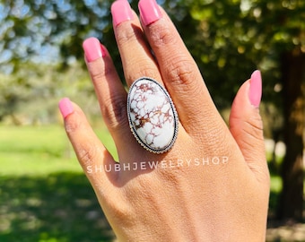 Könnte beinhalten: Ovale Ring mit einem weißen und braunen Stein, gefasst in einem silberfarbenen Metall. Der Ring befindet sich an einer Hand mit rosa Nagellack. Der Text "SHUBHJEWELRYSHOP" ist unten im Bild zu sehen.