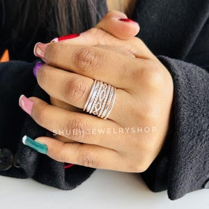 May include: A stack of silver rings with various designs, including braided and textured bands. The rings are worn on a hand with manicured nails. The shop name "SHUBHJEWELRYSHOP" is visible.
