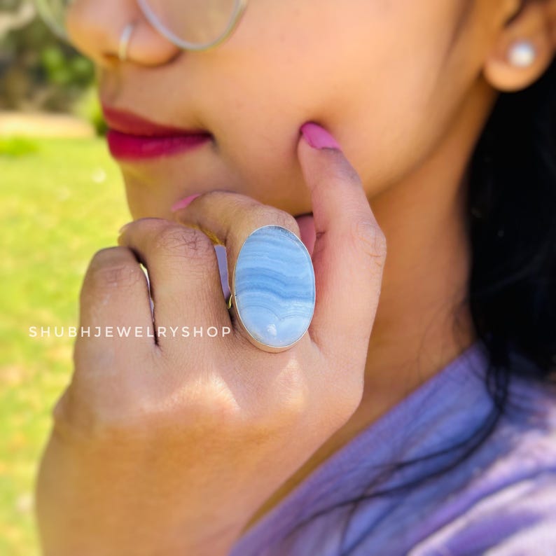 K&ouml;nnte beinhalten: Ovale Ring mit einem gro&szlig;en, hellblauen Stein mit wei&szlig;en Streifen, gefasst in einem silbernen Band. Der Ring wird an einer Hand gezeigt, mit dem Text "SHUBHJEWELRYSHOP" im Bild.