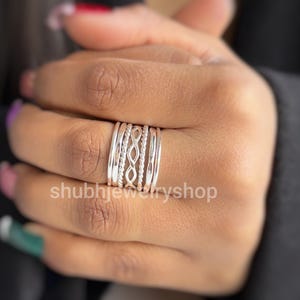 May include: A stackable silver ring set with various designs, including twisted rope and openwork patterns. The rings are worn on a finger, showcasing the different textures and styles. The shop name "shubhjewelryshop" is visible in the image.