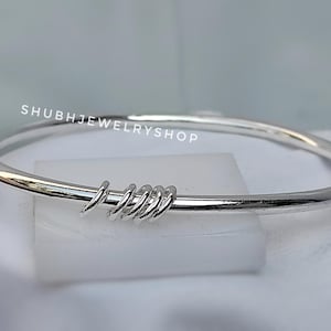 Op de afbeelding: Een zilveren armband met een minimalistisch ontwerp. De armband heeft een gladde, gepolijste band met opgerolde zilveren accenten. De tekst "SHUBHJEWELRYSHOP" is zichtbaar. Dit sieraad is geschikt voor dagelijks gebruik.