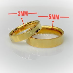 Puede incluir: Se muestran dos anillos dorados, uno de 3 mm y otro de 5 mm de ancho. Los anillos tienen un diseño plano tipo banda. Los anillos están sobre una superficie blanca. El nombre de la tienda "SHUBHJEWELRYSHOP" es visible.