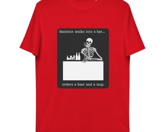 Può includere: T-shirt rosso con grafica quadrata nera. La grafica mostra uno scheletro in un bar con il testo: "Uno scheletro entra in un bar... ordina una birra e un mocio."