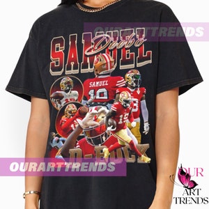 May include: Black t-shirt with a graphic of American football player Deebo Samuel in a red and gold uniform. The design includes the name "SAMUEL" and the number 19. The shirt has a vintage, distressed appearance.