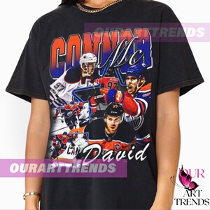 May include: Black t-shirt with a vintage-style graphic of hockey player Connor McDavid. The graphic features a collage of photos of McDavid in action, with the text "Connor McDavid" printed in a bold, colorful font.