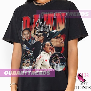 May include: Black t-shirt featuring a collage of images and the name "DAWN Staley" in red and white. The shirt has a vintage, distressed look, with the text "OURARTTRENDS" at the bottom.