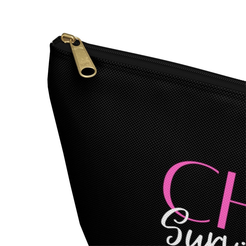 K&ouml;nnte beinhalten: Schwarze Kosmetiktasche mit Rei&szlig;verschluss, mit einem rosafarbenen "Cheers" und einem wei&szlig;en "Sweet"-Text.