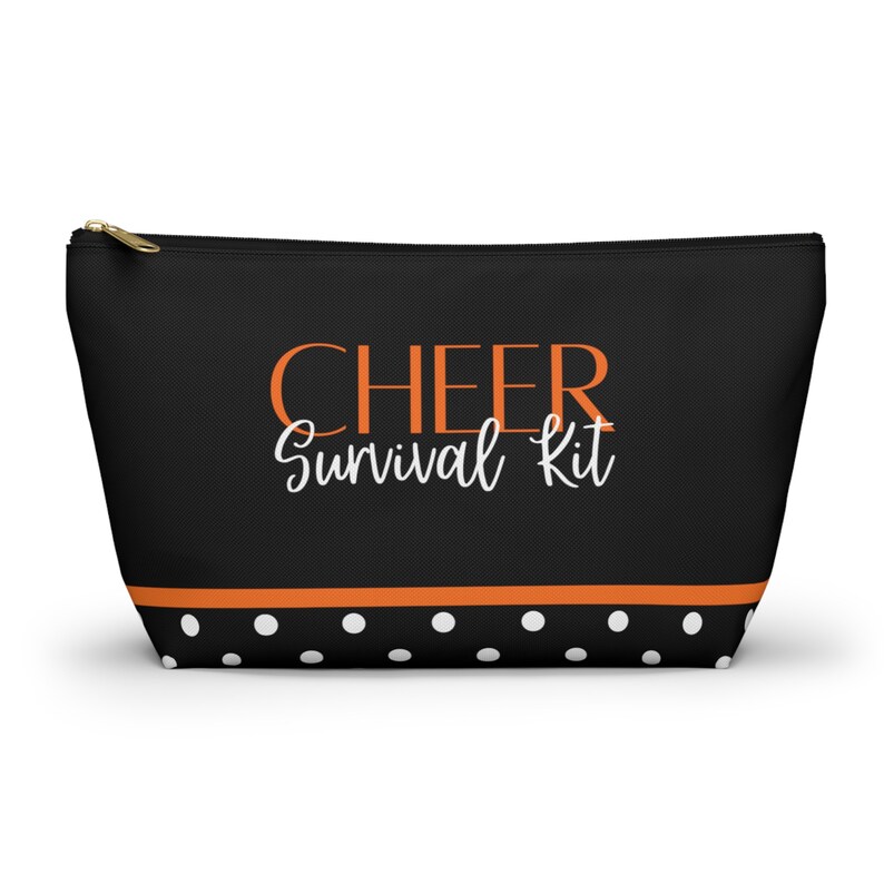K&ouml;nnte beinhalten: Schwarze Kosmetiktasche mit Rei&szlig;verschluss, wei&szlig;em Punktmuster und orangefarbenem Streifen. Die Tasche tr&auml;gt den Schriftzug "CHEER Survival Kit" in orangefarbenen und wei&szlig;en Buchstaben.