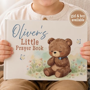 May include: A hardcover book titled Oliver's Little Prayer Book with a white cover featuring a brown teddy bear sitting in a field of flowers with butterflies. A circular badge in the top right corner contains the text girl & boy available.