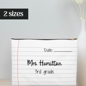 Op de afbeelding: Witte ritszak met een notitieboekpapierontwerp. De tas heeft zwarte lijnen en rode lijnen. De tekst "Date:" staat bovenaan de tas. De tekst "Mrs. Hamilton 3rd grade" staat in het midden van de tas.