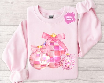 May include: Pink Christmas sweatshirt with a design of three pink and gold glitter ornaments with pink bows.