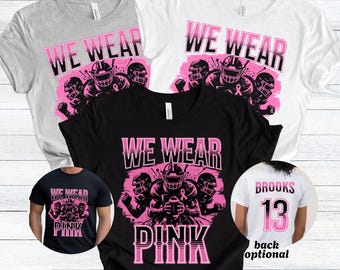 May include: A collection of t-shirts in various colors, including gray, black, and white, with a pink and black graphic. The graphic features football players and the text "WE WEAR PINK". One shirt has the name "Brooks" and the number "13" on the back.