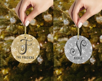 May include: Two round Christmas ornaments with glitter and snowflakes. One is gold with the letter F and "THE FRAZIER'S" text. The other is silver with the letter N and "NICOLE" text.