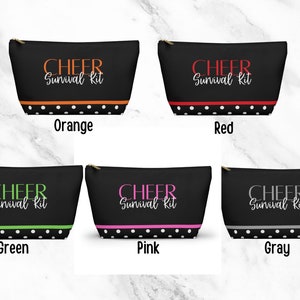 K&ouml;nnte beinhalten: F&uuml;nf schwarze Rei&szlig;verschlusstaschen mit wei&szlig;en Punkten und einem wei&szlig;en Rand. Jede Tasche tr&auml;gt den Text "CHEER Survival Kit" in einer anderen Farbe: orange, rot, gr&uuml;n, rosa und grau.