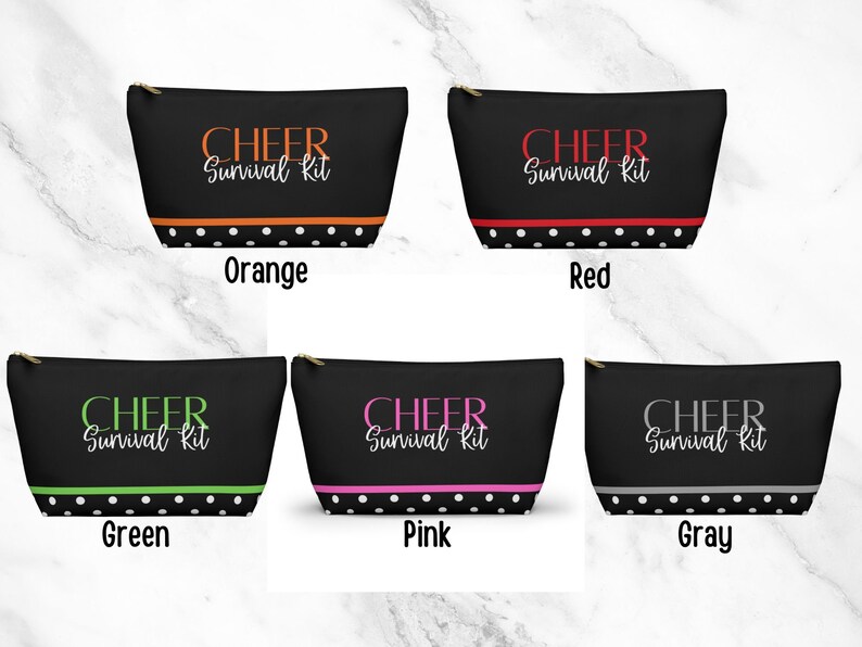 K&ouml;nnte beinhalten: F&uuml;nf schwarze Rei&szlig;verschlusstaschen mit wei&szlig;en Punkten und einem wei&szlig;en Rand. Jede Tasche tr&auml;gt den Text "CHEER Survival Kit" in einer anderen Farbe: orange, rot, gr&uuml;n, rosa und grau.
