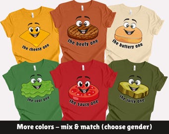 May include: A collection of colorful t-shirts featuring cartoon food characters. The shirts include a yellow "cheesy one", a brown "beefy one", a tan "buttery one", a green "cool one", a red "saucy one", and an olive green "juicy one".
