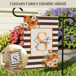 May include: Double-sided garden flag with a fall theme. The flag features a white background with brown stripes, an orange letter "S", and the name "Smith" in script. Pumpkins and flowers decorate the flag. The text "Custom Colors" is at the top.