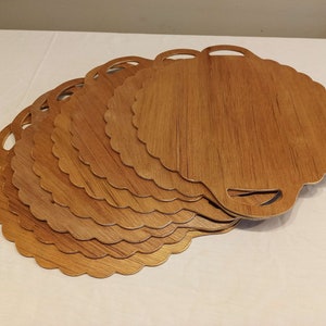 May include: A stack of seven wooden serving trays with a scalloped edge and a handle cutout. The trays have a light brown wood grain finish and are arranged in a fan shape, showcasing their design.