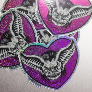 May include: A set of four heart-shaped stickers with a glittery purple background. Each sticker features a black and white illustration of a bat with the text "batricia" printed below. The stickers are from the website "spookcult.com".
