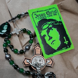 May include: A rosary with green beads, silver accents, and a crucifix. A green card with the text "Jesus Christ LOOKS LIKE ME" and a black illustration of Jesus is next to the rosary.