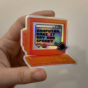 May include: A holographic sticker shaped like an orange vintage computer monitor and keyboard. The screen displays the text "COMPUTAH, MAKE IT GAY AND SPOOKY" with a pixelated rainbow heart and a small orange pumpkin icon, plus a black cursor arrow.