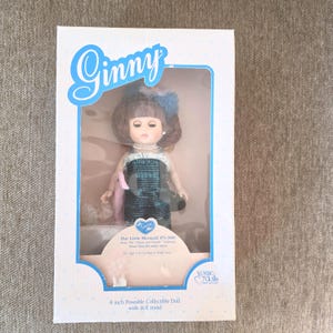 K&ouml;nnte beinhalten: Eine Sammler-Ginny-Puppe in einer Box. Die Puppe hat braunes Haar, eine blaue Schleife und ein t&uuml;rkis-schwarzes Kleid. Auf der Box steht "Ginny" in blauer Schrift und "Our Little Mermaid #71-3060". Die Puppe ist 20 cm gro&szlig;.
