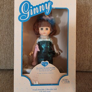 K&ouml;nnte beinhalten: Eine Vintage-Ginny-Puppe in ihrer Originalverpackung. Die Puppe tr&auml;gt ein gr&uuml;nes Paillettenkleid und hat auburnfarbenes Haar mit einem blau-braunen Haarschmuck. Auf der Box steht "Our Little Mermaid" und "8 inch Poseable Collectible Doll".