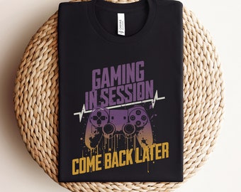 May include: Black t-shirt with a purple and yellow graphic of a video game controller and the text "Gaming in Session Come Back Later".