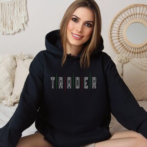 May include: Black hooded sweatshirt with the word "TRADER" printed in white with green and red accents.