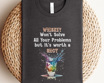 May include: A dark gray t-shirt with the text "Whiskey Won't Solve All Your Problems but it's worth a Shot" in white and gold lettering. A colorful illustration of a shot glass with a splash of liquid is below the text.