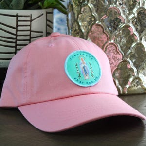 May include: Pink baseball cap with a blue and green patch that says "The  Mother  Pray For Us" with a picture of the Virgin Mary.