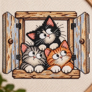 May include: A cross-stitch embroidery piece featuring three kittens looking out of a wooden window frame. One kitten is black, one is grey tabby, and one is orange tabby. All three have large white eyes, pink ears, and white paws resting on the sill.