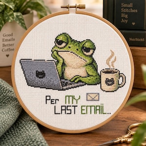 May include: A circular wooden embroidery hoop containing a cross-stitch design of a green frog sitting at a grey laptop with a steaming mug. The text reads "PER MY LAST EMAIL..." in black and green letters, accompanied by a small envelope icon.