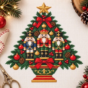 May include: A cross-stitch pattern of a Christmas tree featuring three nutcracker figures in blue, red, and green uniforms. The tree is decorated with red bows, gold and red ornaments, and pinecones, topped with a gold star and set in a base.