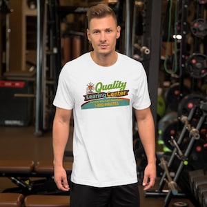 Könnte beinhalten: Weißes T-Shirt mit dem Text "Quality Learning Center" in Grün und Braun, mit einer Cartoon-Grafik. Darunter steht "For Kids Who Can't Read Good" und "1-800-PIRATES" in Blau. Das Shirt hat kurze Ärmel.