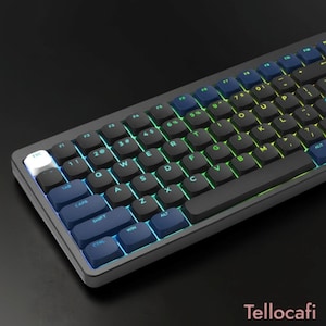 Puede incluir: Un teclado mecánico con marco gris oscuro y teclas negras con retroiluminación verde. La tecla escape es blanca, mientras que las teclas de función, tabulador, bloqueo de mayúsculas, shift, control y windows son azul oscuro. Texto Tellocafi visible.