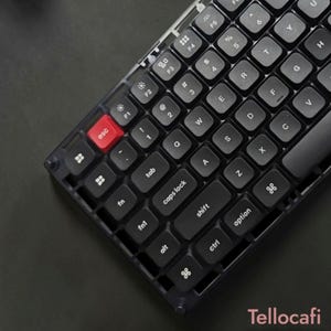 Może przedstawiać: Czarna klawiatura mechaniczna z półprzezroczystą ciemną ramką i czarnymi klawiszami z białymi literami. Klawisz escape jest w jednolitym czerwonym kolorze. Układ zawiera standardowe klawisze funkcyjne, modyfikujące i alfanumeryczne.