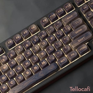 May include: A computer keyboard featuring dark brown wood grain keycaps with gold-colored lettering. The keys include standard alphanumeric characters, function keys labeled F5 through F12, and a long space bar. The text Tellocafi is visible.