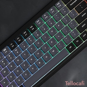 Può includere: Una tastiera meccanica compatta con tasti grigio scuro, lettere bianche e una vivace retroilluminazione RGB che illumina gli spazi tra i tasti. Il layout include caratteri alfanumerici, tasti funzione e la parola Tellocafi.